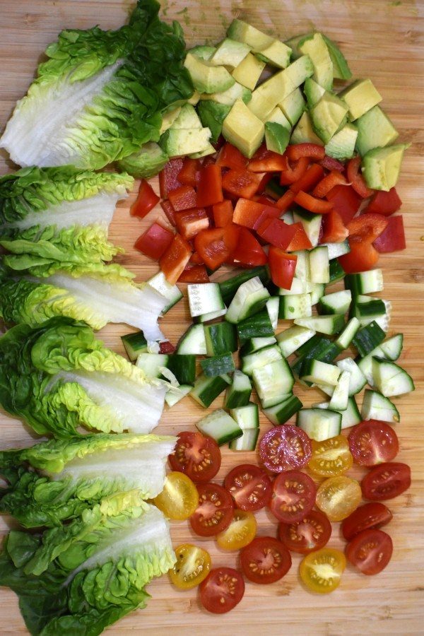 salad leaves alongside chopped avocado, red bell peppers, cucumber and cherry tomatos