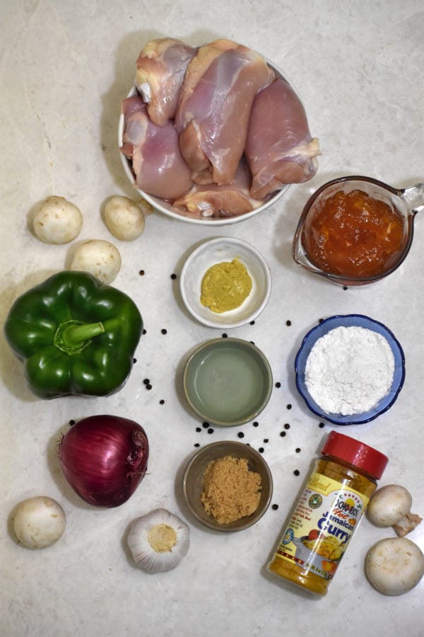 overhead ingredient picture depicting, clockwise from top, chicken, apricot preserves, flour, curry powder, mushrooms, brown sugar, white vinegar, red onion, green pepper and mustard arranged on a marble surface