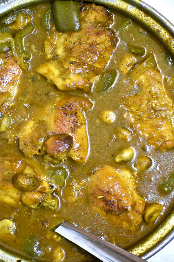 overhead shot of south african chicken curry in an electric skillet with a large spoon sticking out of it